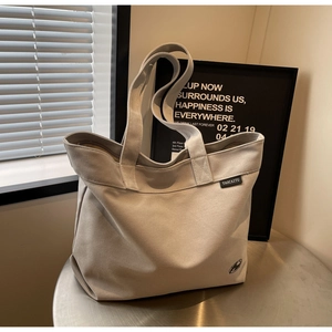 Detalle de bolso tote de lona gris con asas reforzadas y logotipo sobre mesa metálica