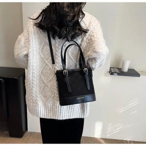 Detailansicht einer schwarzen Stepp-Beuteltasche an Model mit cremefarbenem Strickpullover