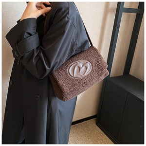 Detail of plush brown shoulder bag featuring leather M logo patch and slim strap