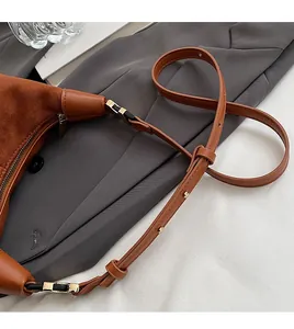 Detail of brown matte shoulder bag featuring an adjustable leather strap with gold rivets