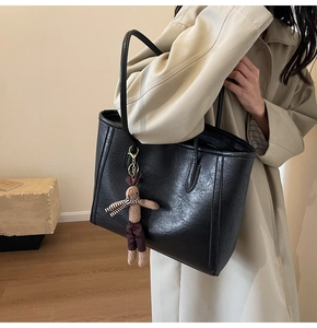 Detail of black faux leather tote bag with plush bunny charm on a beige trench coat