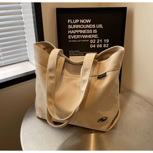 Detalle de bolso tote de lona con etiqueta tejida sobre una mesa metálica minimalista