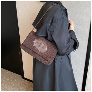 Detail of a dark brown fuzzy tote bag with 3D oval leather logo worn as an underarm bag