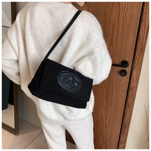 Close-up of black lamb wool shoulder bag with circular leather logo and strap detail