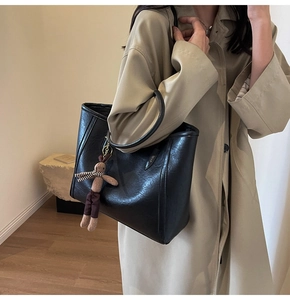 Large black leather tote bag with rabbit charm shown on model in a beige coat