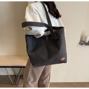 Detalle del bolso tote de lona gris oscuro con logo naranja y correa de hombro