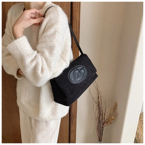 Detail of black faux fur shoulder bag with leather M logo patch and slim strap