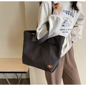 Detalle del bolso tote grande de lona gris oscuro con etiqueta tejida y correa ancha