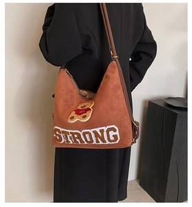 Detail view of brown faux suede hobo bag with teddy bear patch and Strong text