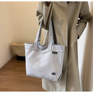 Detalle de bolso tote de lona beige de gran capacidad usado con una gabardina elegante