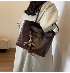 Large dark brown leather tote bag with rabbit charm worn over a beige trench coat