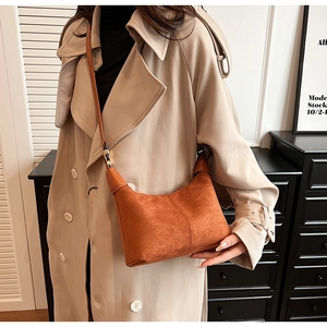 Close-up of brown suede crescent crossbody bag worn by a model in a modern interior
