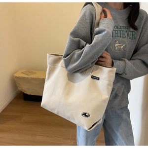 Detalle del bolso tote de lona beige con etiqueta de marca en el lateral de la modelo