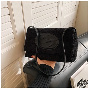 Close-up of black plush shoulder bag with leather M logo and thin leather straps