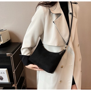 Chic black matte suede crescent bag with gold buckle on a stylish white trench coat