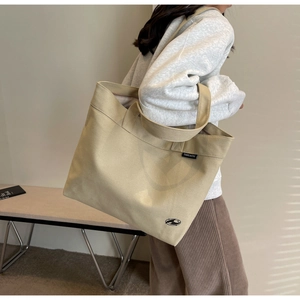 Detalle del bolso tote de lona beige con etiqueta de logo y textura en el modelo