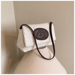 Detailed view of plush white shearling texture and brown leather logo patch on shoulder bag