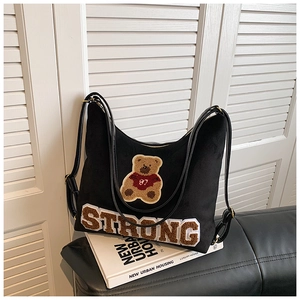 Close-up of black matte shoulder bag featuring 'STRONG' embroidery and brown bear patch