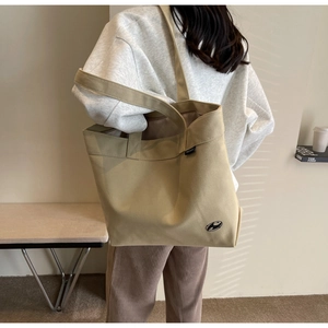 Detalle del bolso tote de lona caqui con bordado negro y asas largas para hombro