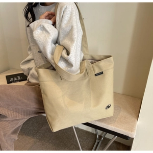 Vista detallada del bolso tote de lona beige con asas dobles y etiqueta de la marca