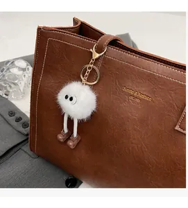 Porte-clés monstre en peluche à grands yeux sur un sac fourre-tout en cuir marron et détails dorés