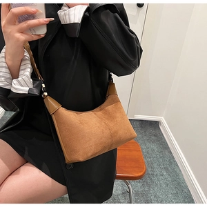 Detail of brown faux suede crescent shoulder bag with dark brown leather piping and strap