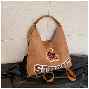 Detail of embroidered teddy bear and STRONG lettering on a brown frosted leather bag
