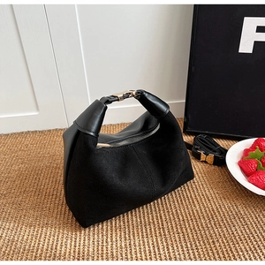 Detail of black matte crescent bag with gold clasp and strap on a woven surface