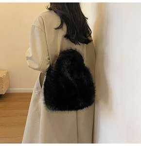 Détail d'un sac en peluche noir en forme de cœur avec une chaîne en argent porté par un mannequin