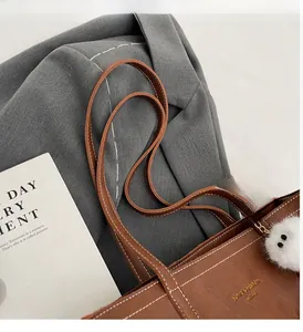 Sac cabas en cuir marron avec surpiqûres et bijou de sac en peluche sur une veste grise