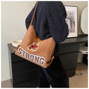 Detail of brown suede tote bag featuring strong embroidery and a teddy bear patch
