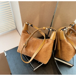 Close-up of brown suede shoulder bag with leather trim and adjustable buckle strap