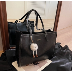 Détail du sac cabas noir avec logo doré, surpiqûres et pendentif en peluche blanche