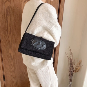 Minimalist black plush shoulder bag with large B logo held by model in home setting