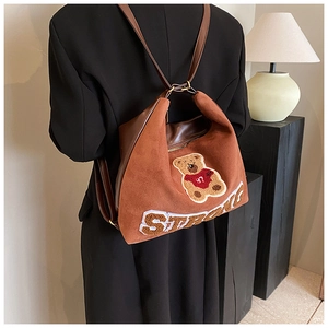 Detail view of brown faux suede backpack featuring a plush bear patch and leather straps