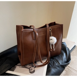 Détail d'un sac cabas en cuir marron foncé avec surpiqûres blanches et charme peluche