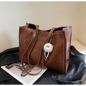 Détail du sac cabas en cuir marron avec surpiqûres blanches et breloque monstre