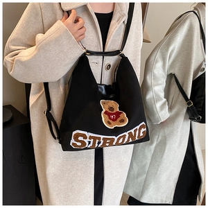 Detail of black tote bag featuring a teddy bear patch and plush STRONG lettering embroidery