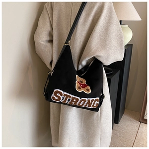 Detail of black canvas shoulder bag featuring a fuzzy teddy bear patch and Strong embroidery