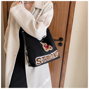 Detail of plush bear embroidery and STRONG lettering on a black canvas shoulder bag