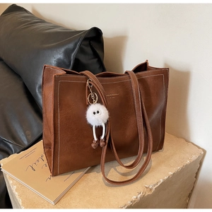 Détail d'un sac cabas marron en cuir avec un porte-clé en fourrure et un logo