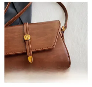 Détail de la texture en cuir PU marron et des pieds de protection dorés du sac