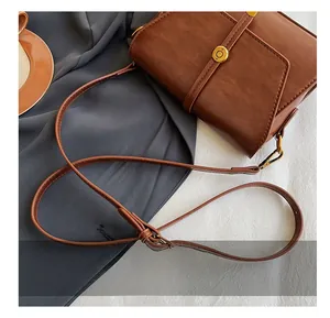 Détail de la bandoulière réglable en cuir marron et boucles dorées du sac à main rétro