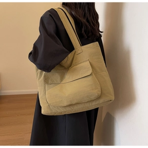 Detail of khaki nylon tote bag featuring a large front flap pocket shown on a model