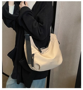 Macro detail of a beige nylon crescent bag featuring a black wide strap and zipper detail