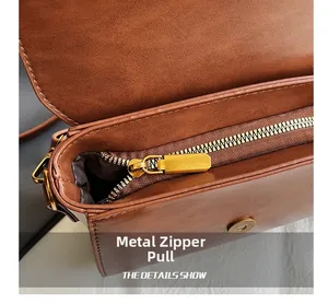 Détail de la fermeture éclair dorée et du cuir marron texturé sur le sac bandoulière