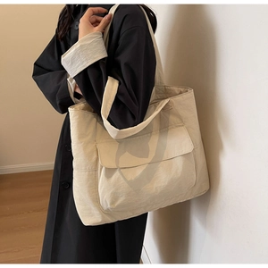 Detail of a large beige nylon tote bag with front flap pocket styled with a black trench coat