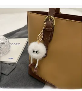 Detail of white fluffy plush keychain with eyes on a brown leather tote bag