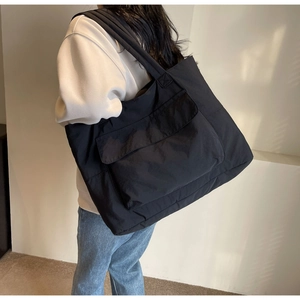 Close-up of a large black nylon tote bag with front pocket carried by a model