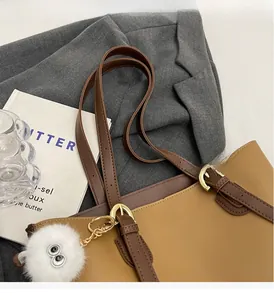 Detailed close-up of large brown tote bag with plush monster charm and metal hardware